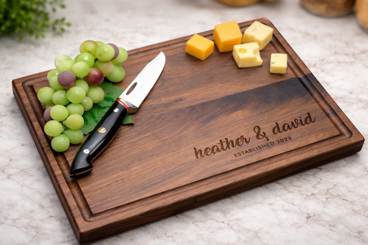 Engraved wooden cutting board with grapes, cheese cubes, and a kitchen knife.