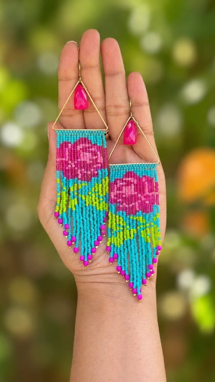 Colorful beaded earrings with pink floral patterns held in a person's hand.