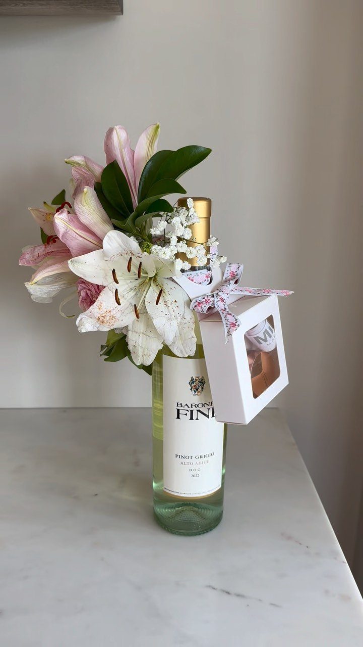 Wine bottle decorated with pink and white lilies and a small gift box.