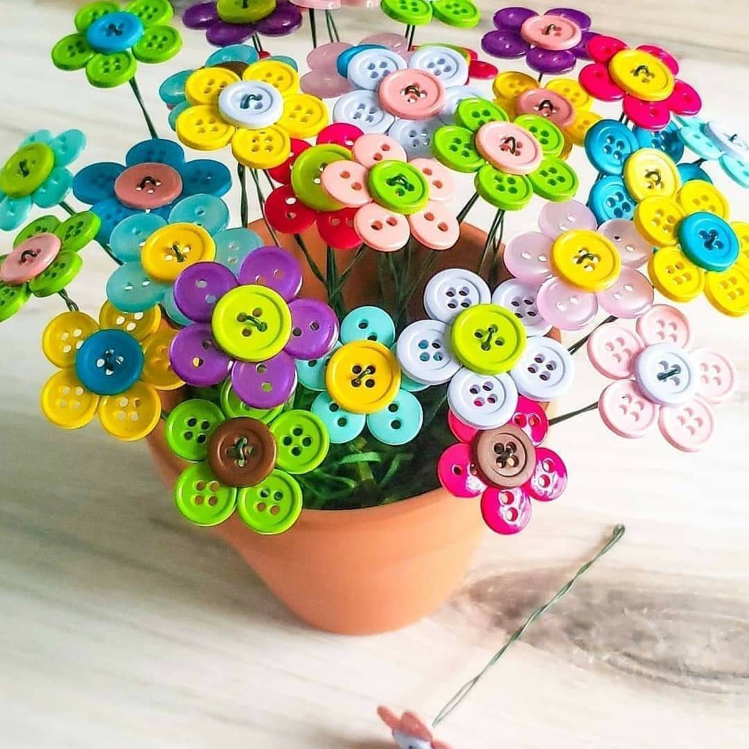 Colorful button flowers arranged in a small terracotta pot on a white surface.