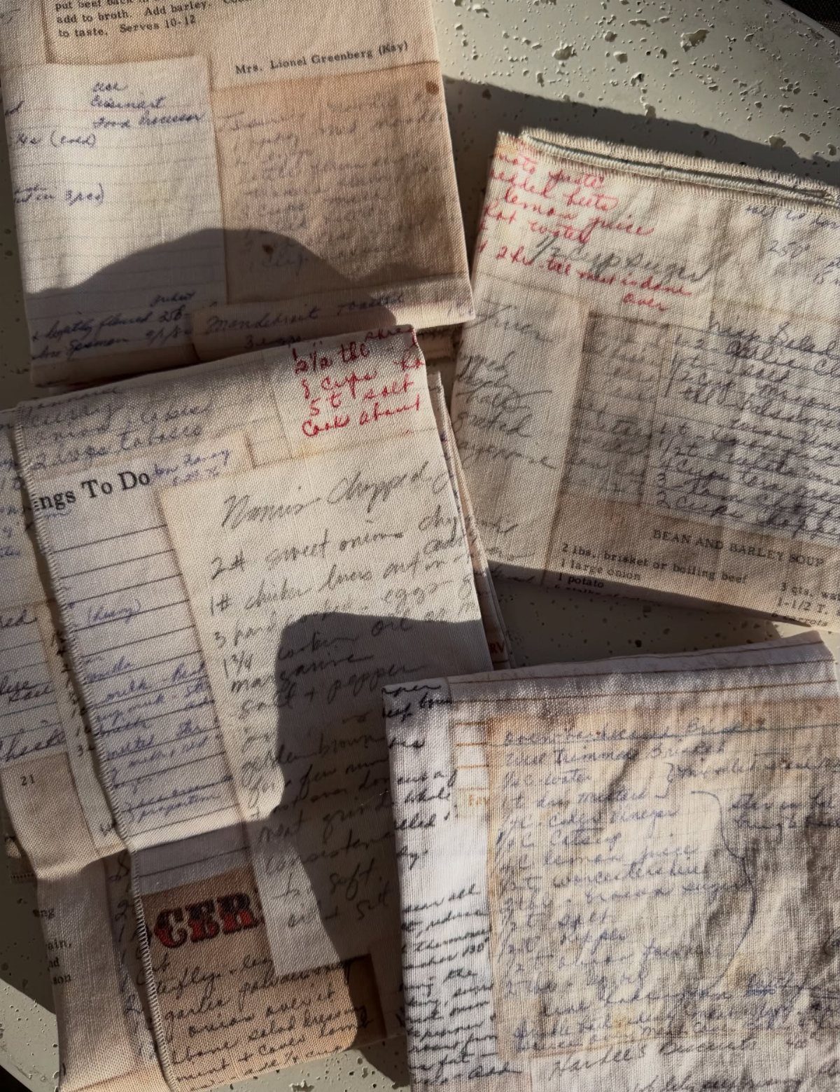 Folded off-white fabric towels printed with handwritten family recipes and notes.