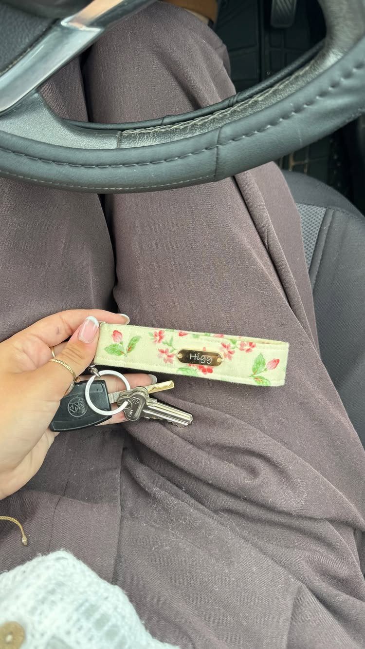 Floral fabric keychain with keys held by a hand against brown trousers.