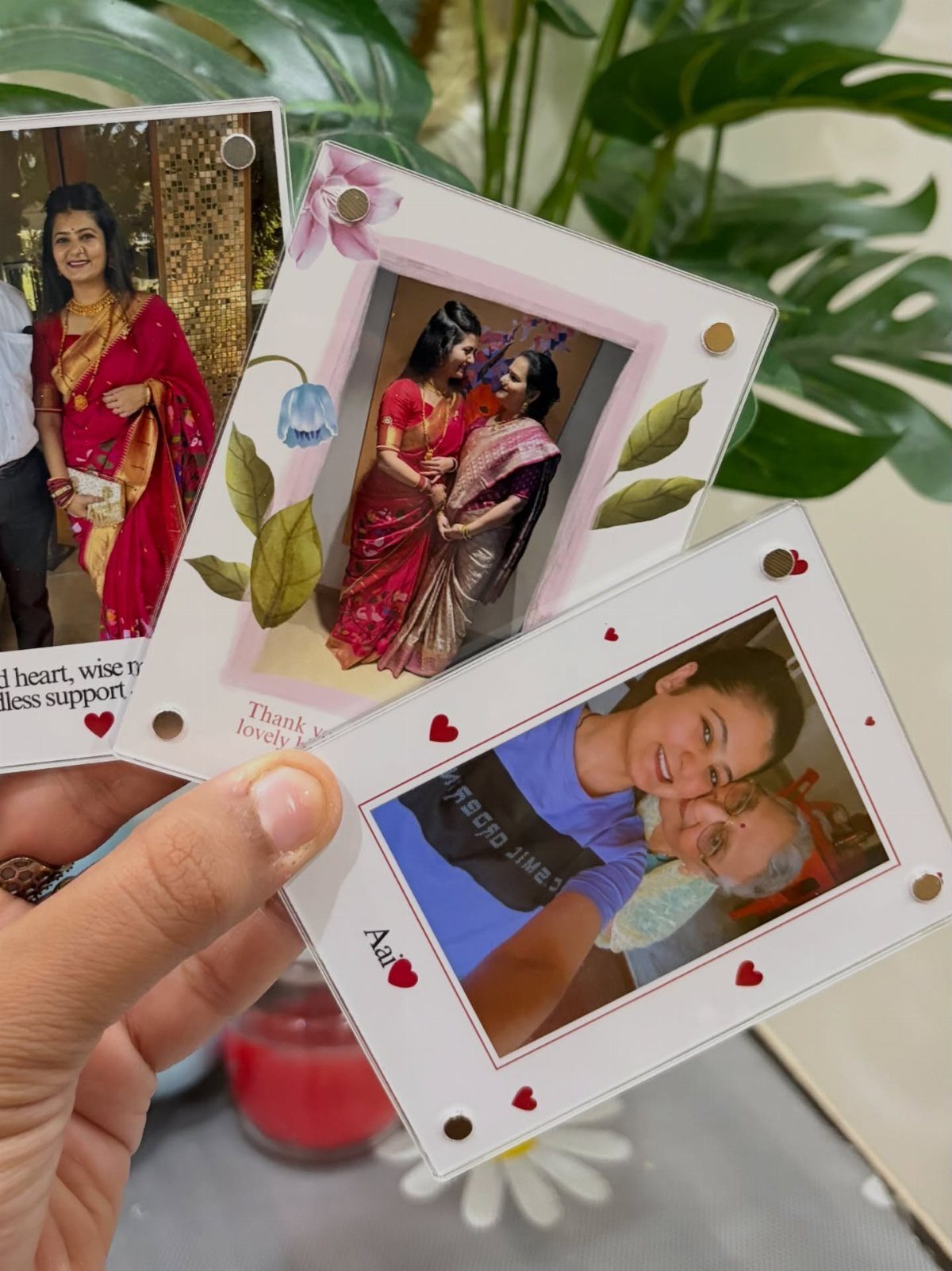 Hand holding three small decorated photo frames with pictures of women and hearts.