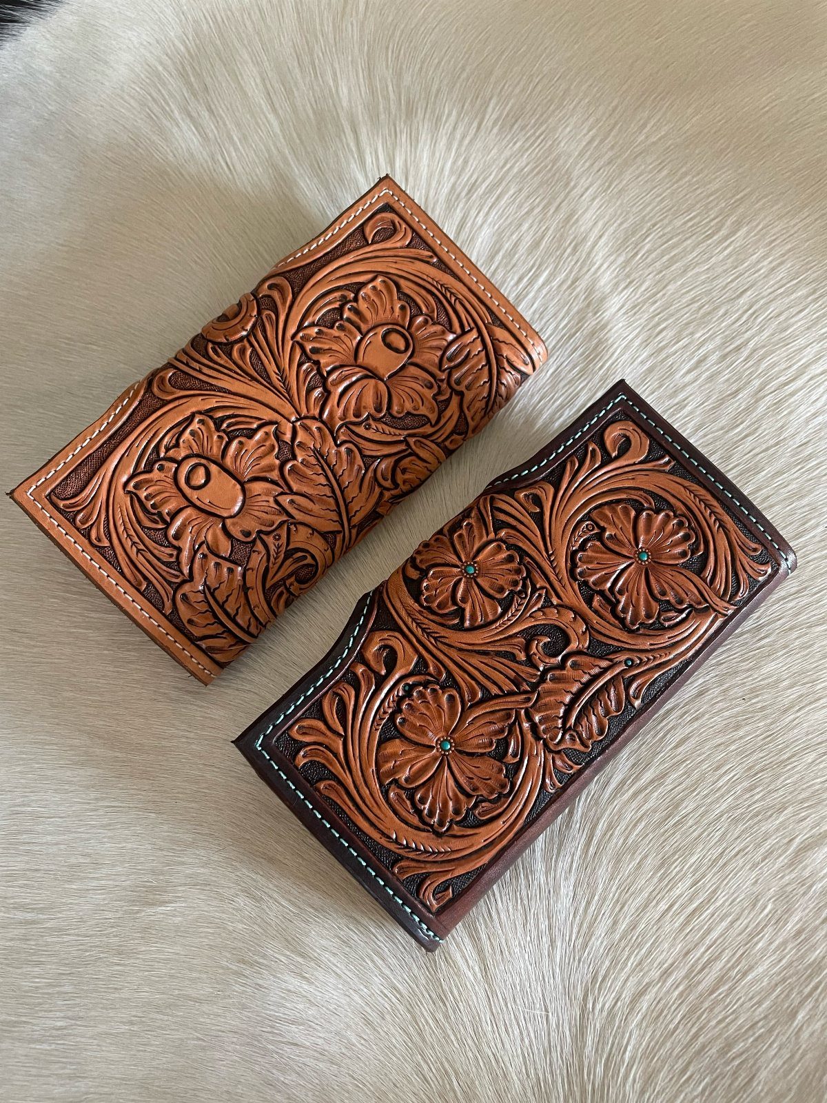 Two hand-tooled leather wallets with floral carvings on a white fur background