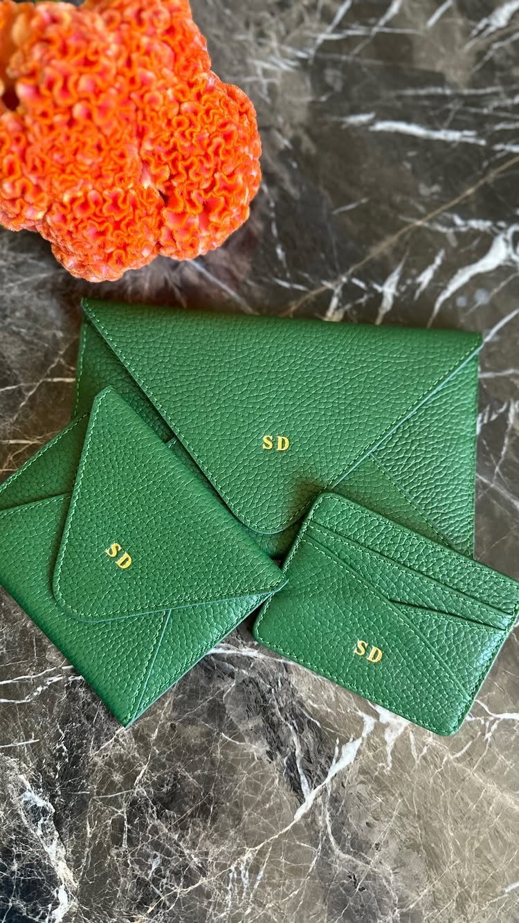 Green leather envelope clutch and matching accessories with gold initials on marble surface