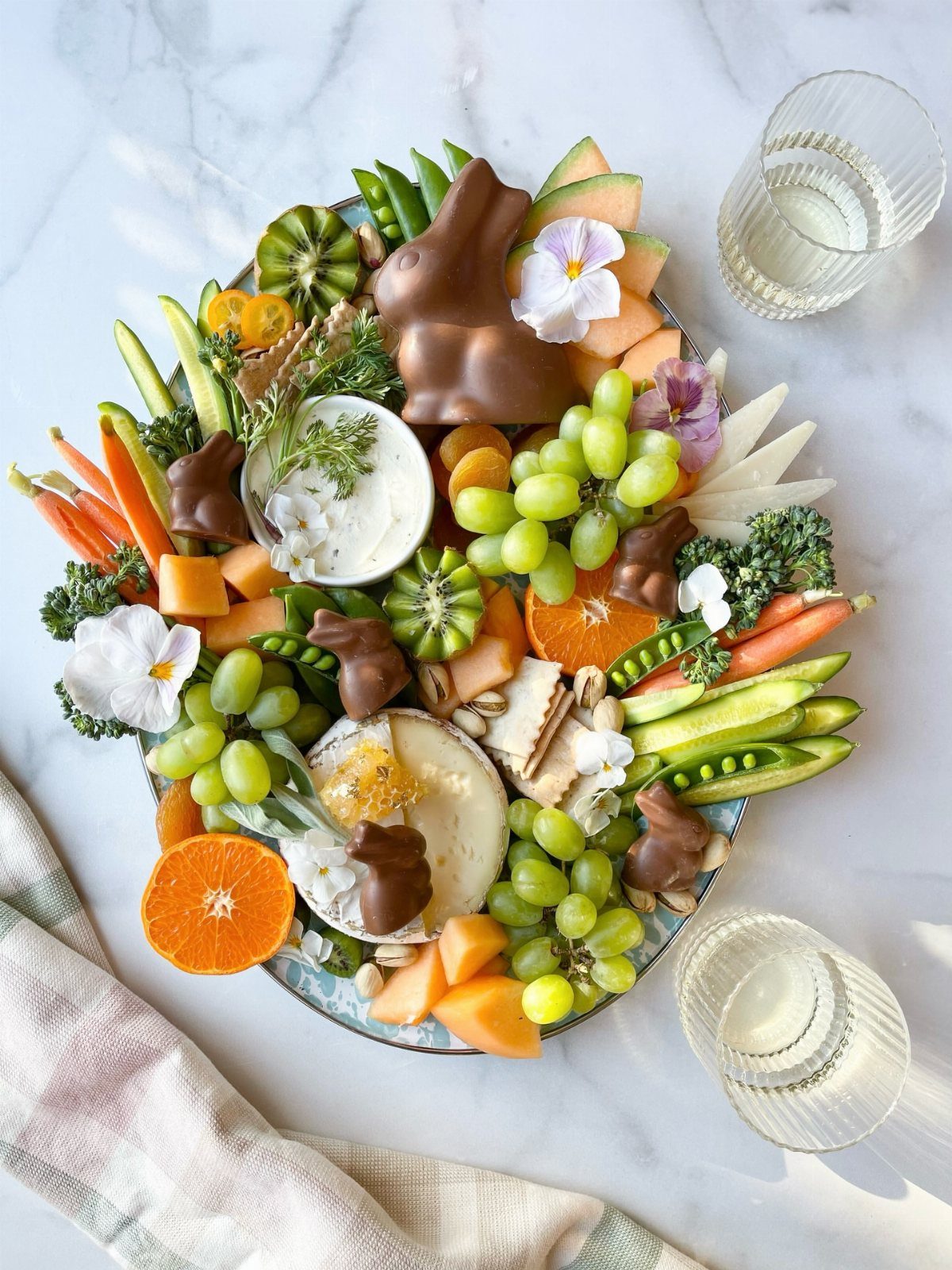 Easter charcuterie board with a large chocolate bunny, fresh fruits, vegetables, and cheese.