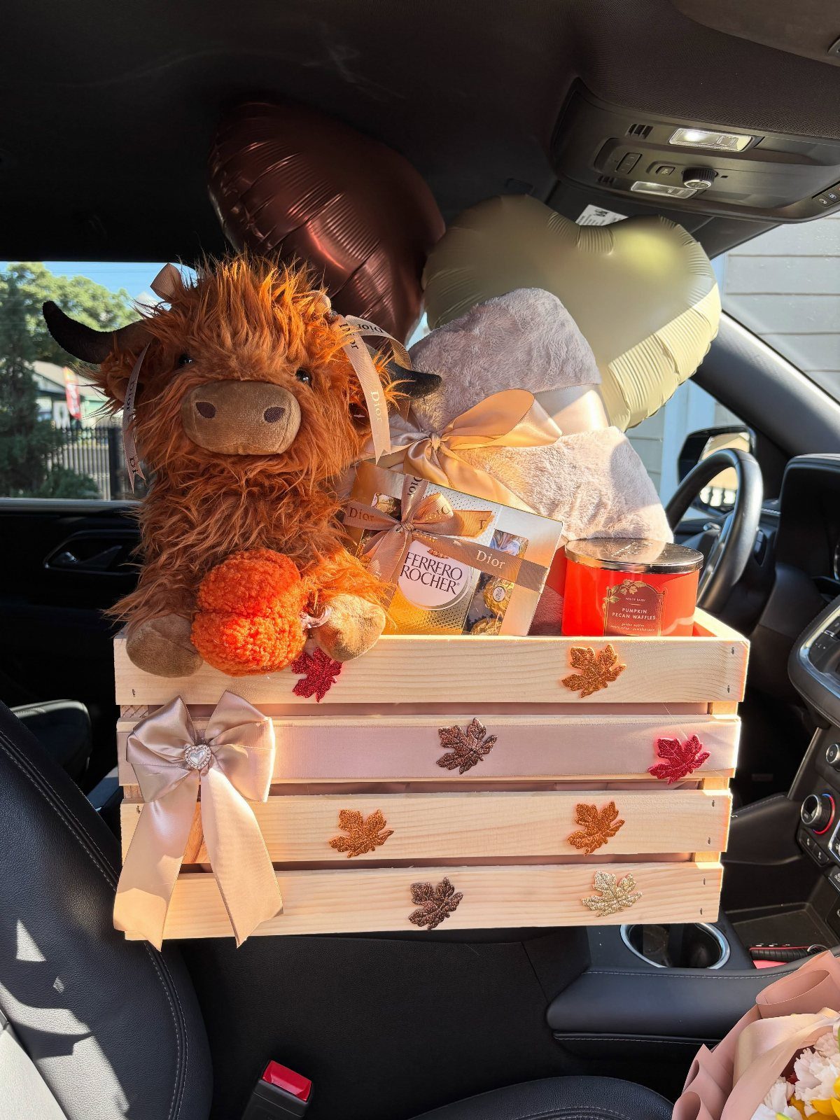 Gift crate with plush cow and balloons sitting on a car seat
