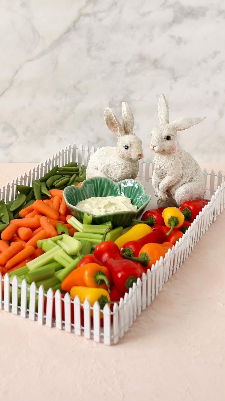 Vegetable tray with a white picket fence border and two white rabbit figurines.