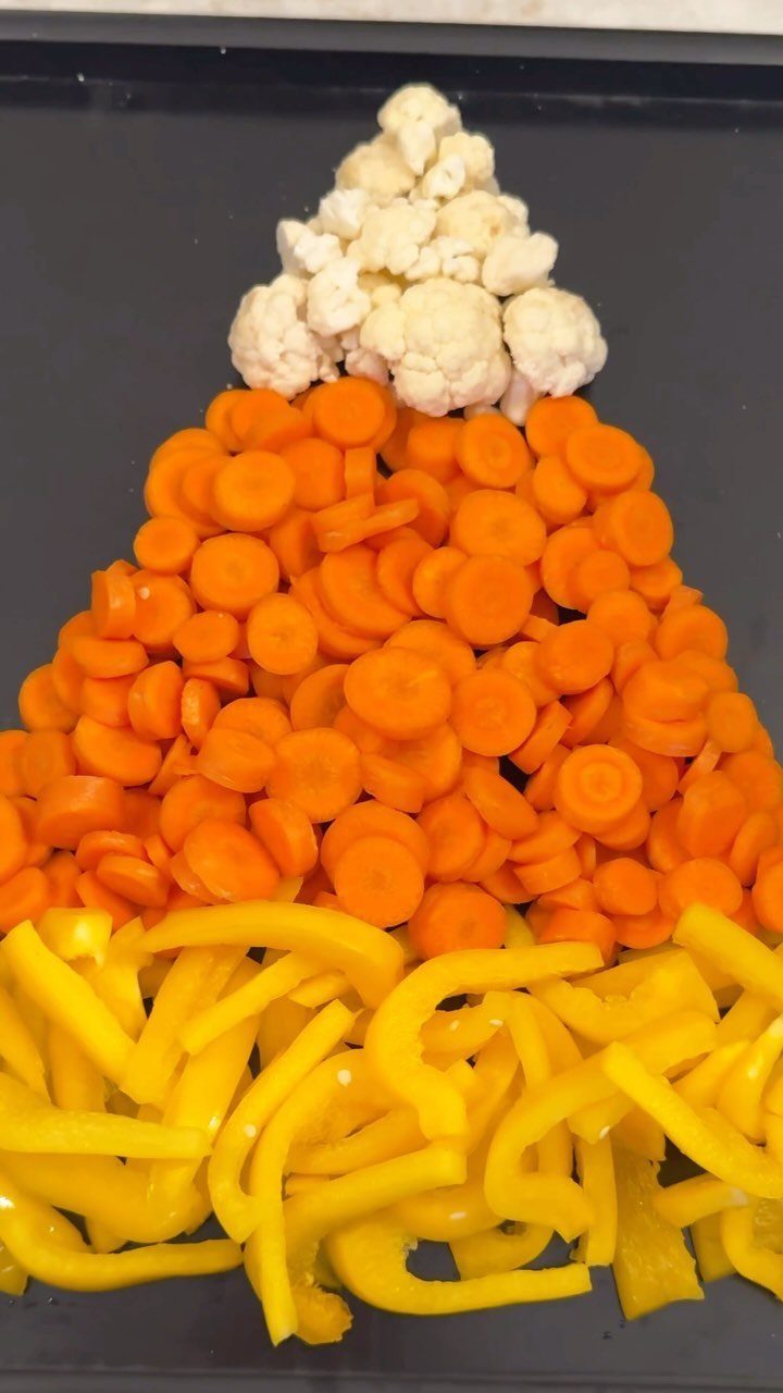 Candy corn shaped veggie tray with cauliflower, carrots, and yellow bell peppers.