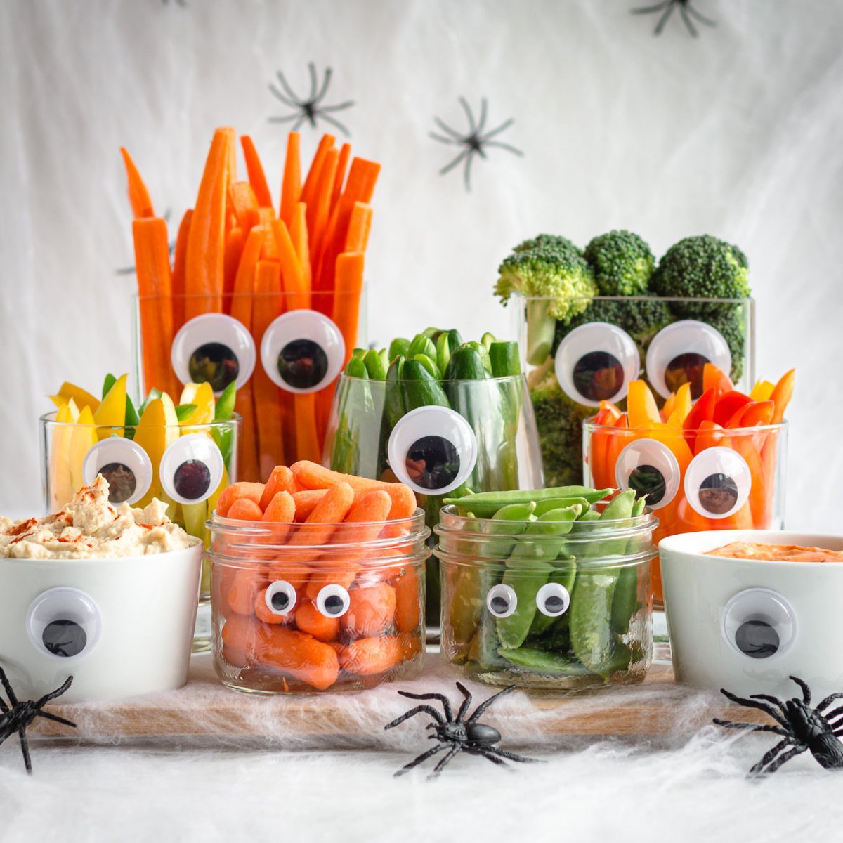 Vegetable sticks in jars with googly eyes and plastic spiders on white webbing.