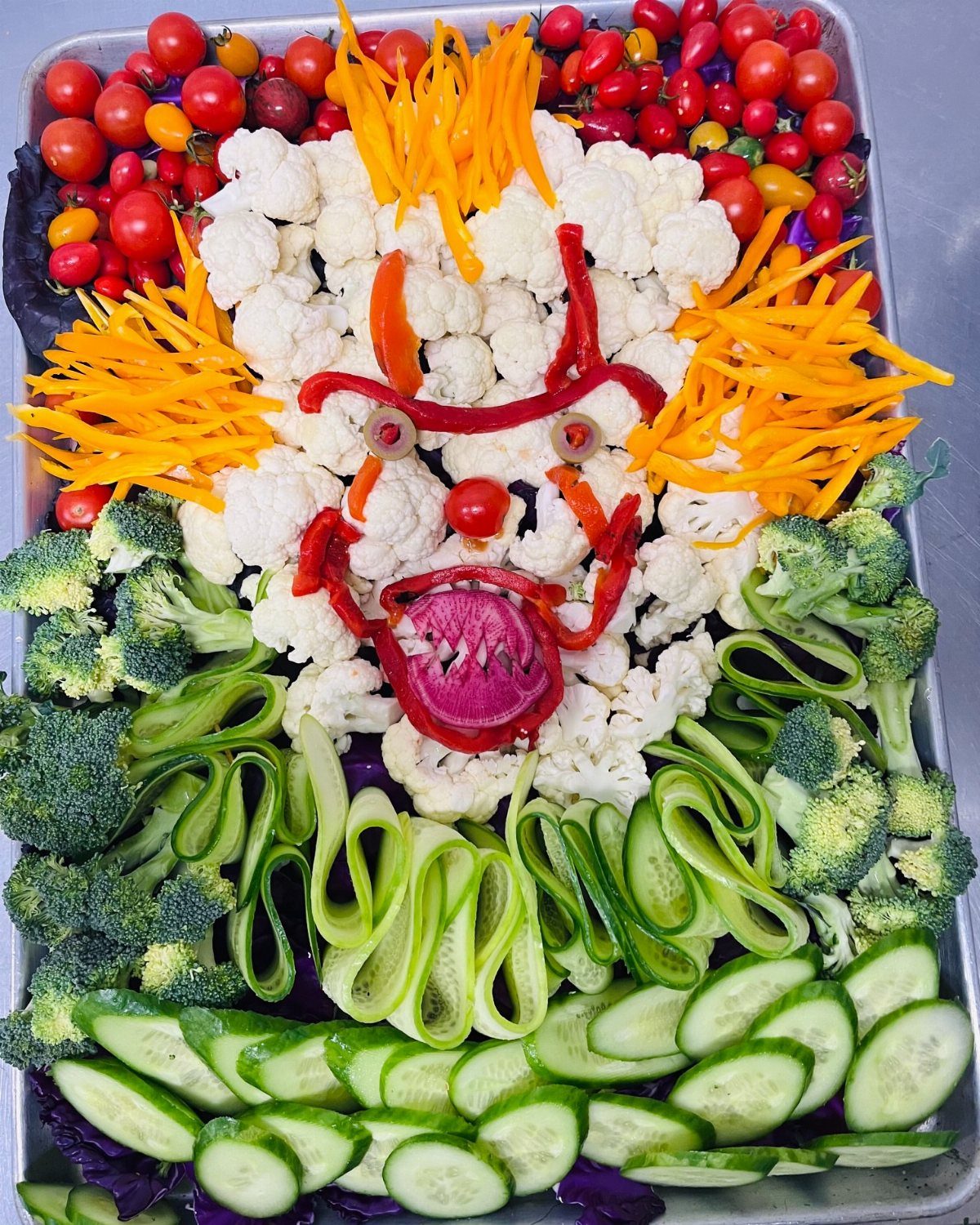 Vegetable platter arranged as a face with cauliflower, carrots, broccoli, and cucumbers.