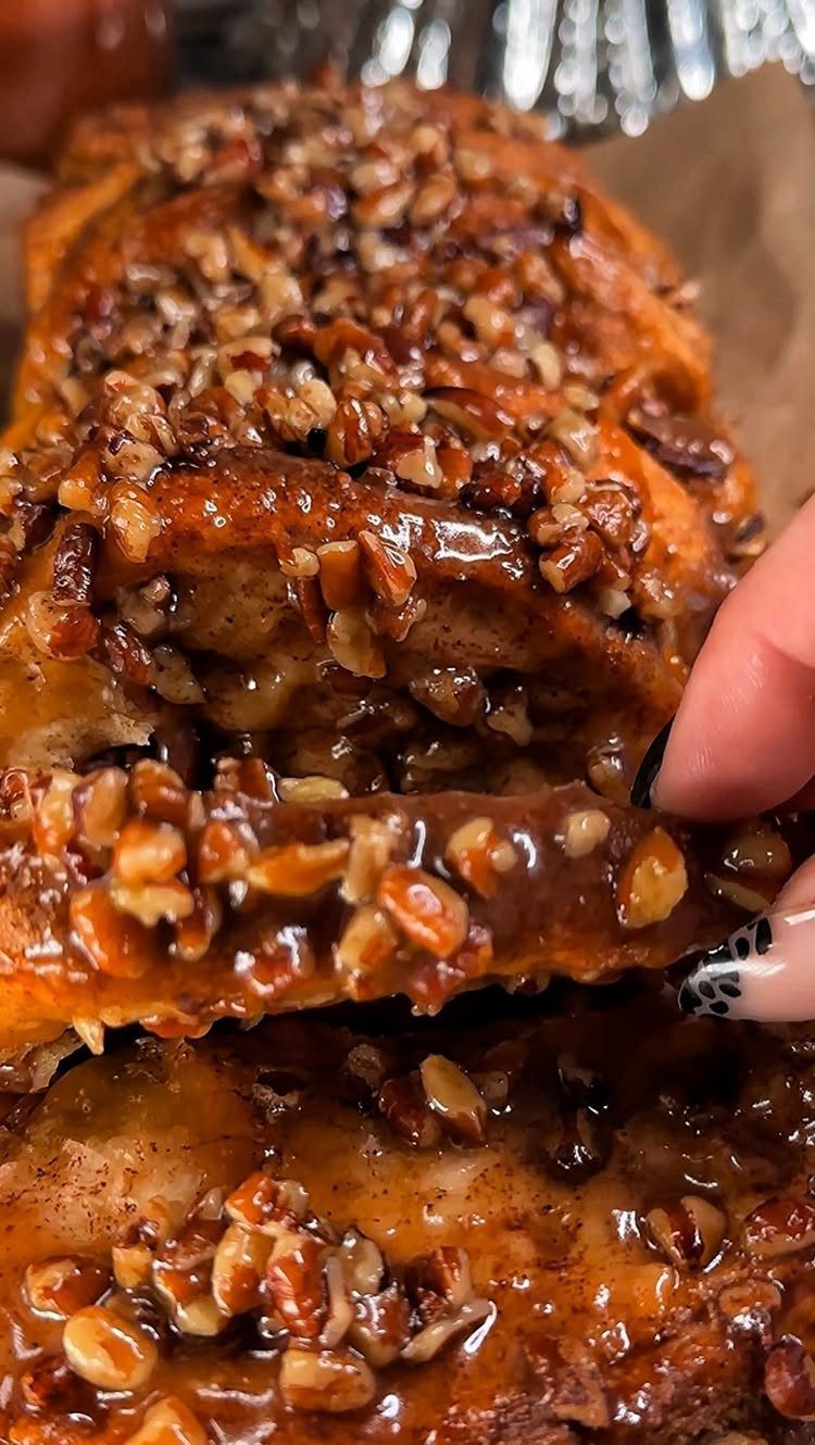 Glazed cinnamon sweet bread topped with pecans being pulled apart by a hand.