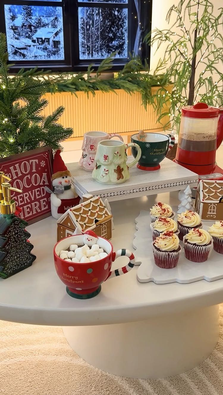 Hot cocoa with marshmallows, red velvet cupcakes, and festive mugs on a table.