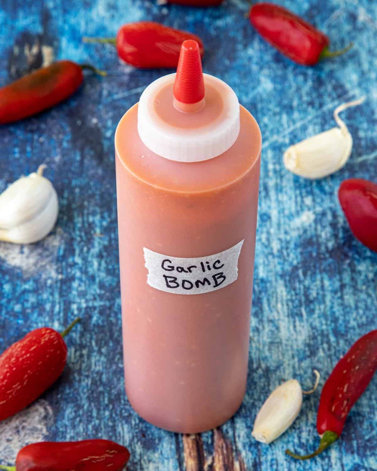 Squeeze bottle of Garlic Bomb hot sauce surrounded by red chilies and garlic cloves.