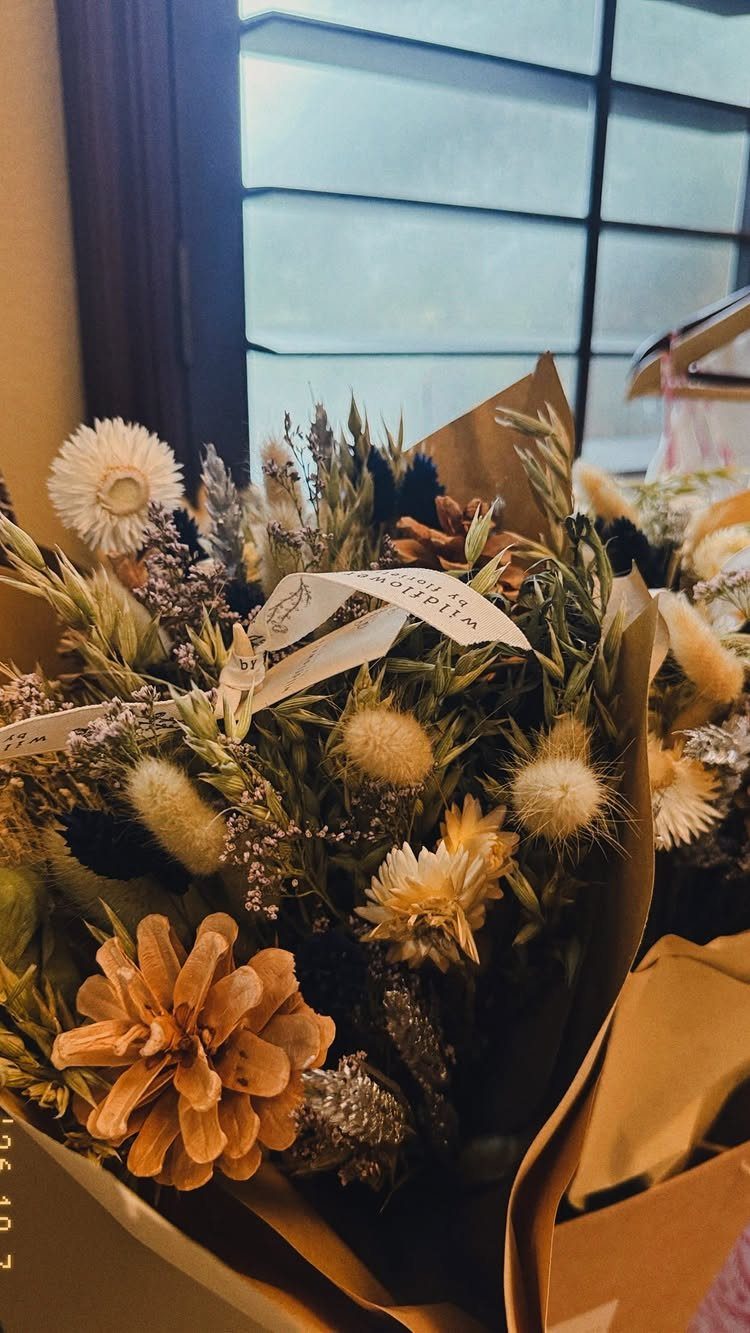 Dried flower bouquet in neutral tones wrapped in brown kraft paper with ribbon