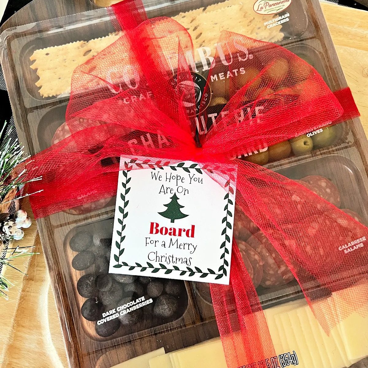 Charcuterie gift tray with red ribbon and Christmas tag on a wooden surface