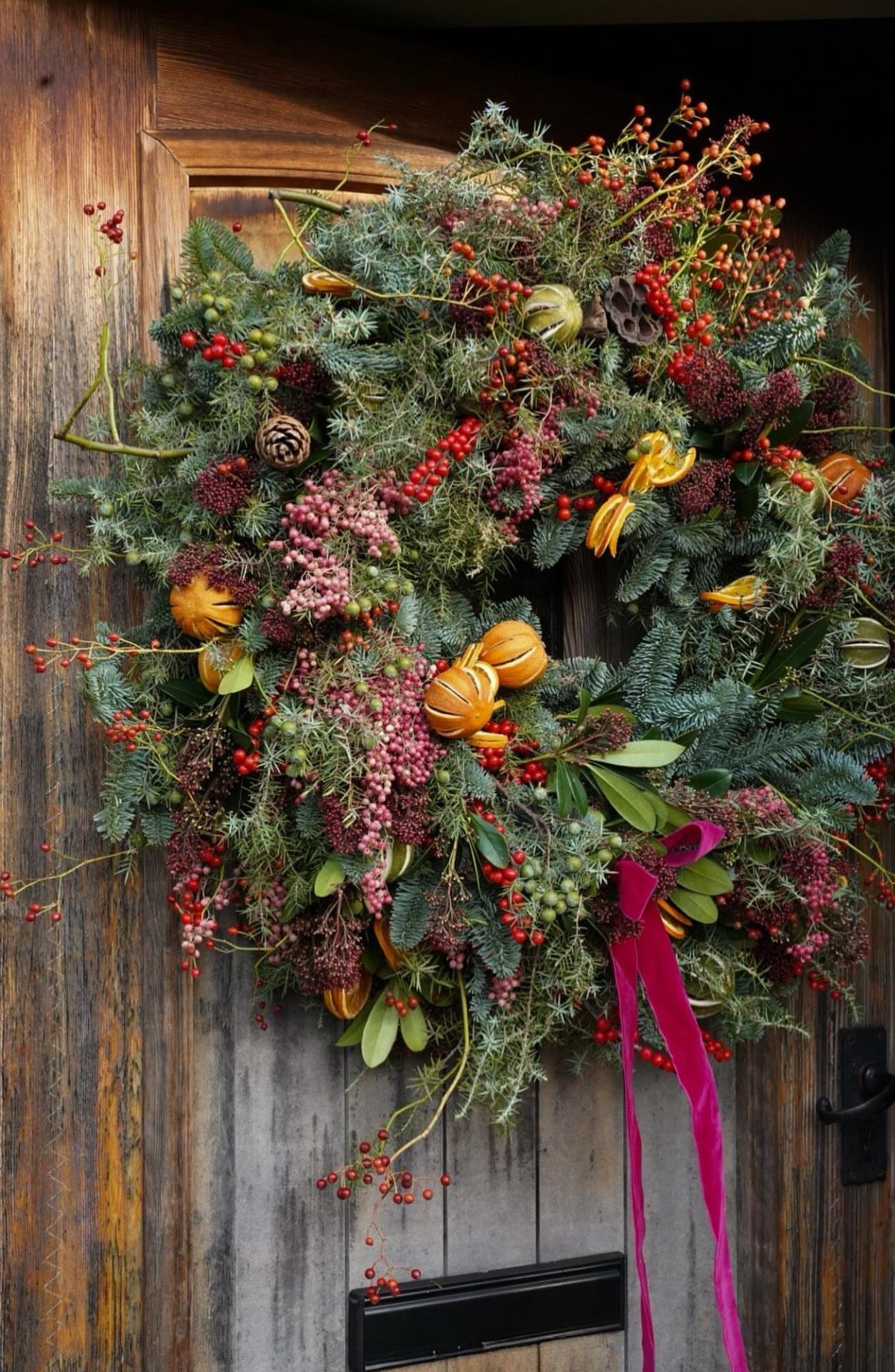 Christmas wreath with evergreen branches, red berries, and orange slices on wooden door
