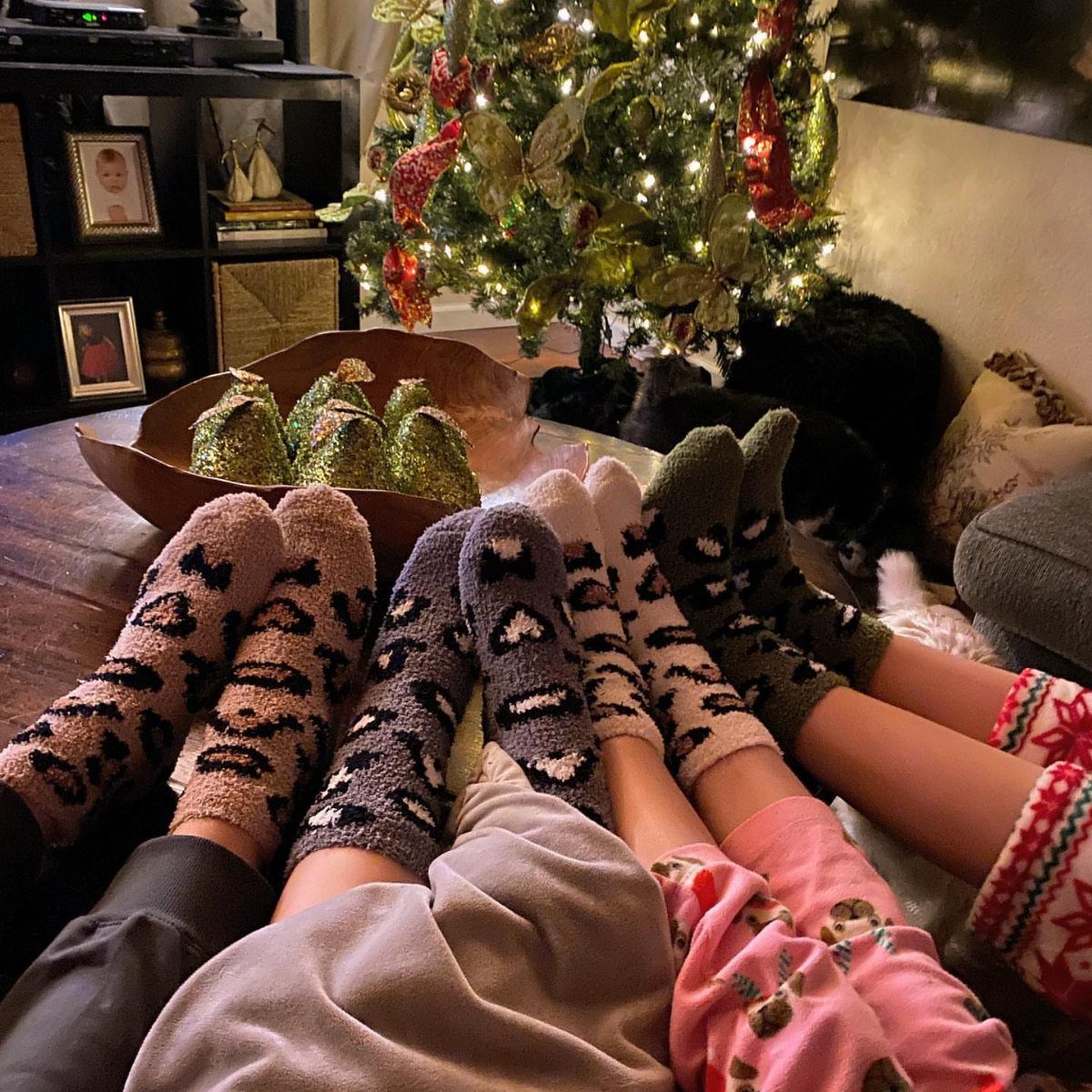 Feet wearing patterned fuzzy socks resting on a table near a Christmas tree.