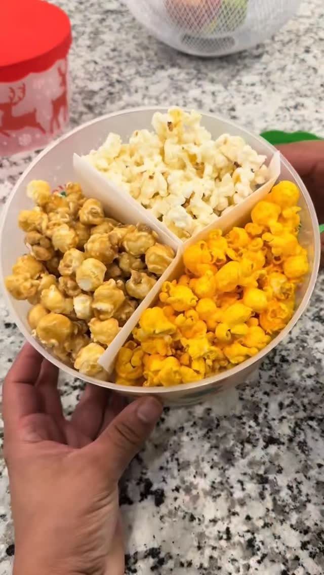 Three varieties of gourmet popcorn in a divided clear plastic container held by hand.