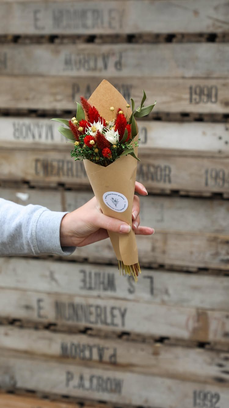 Small bouquet of red and white flowers wrapped in brown paper held by hand.