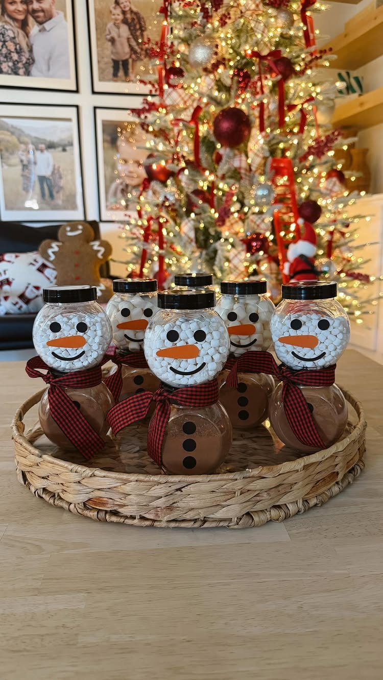 Mason jars decorated as snowmen in a wicker tray before a Christmas tree