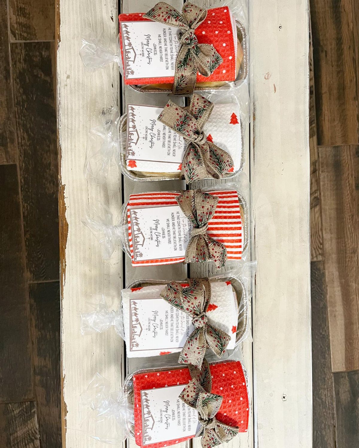 Five wrapped baked good gift containers with red fabric and brown bows.
