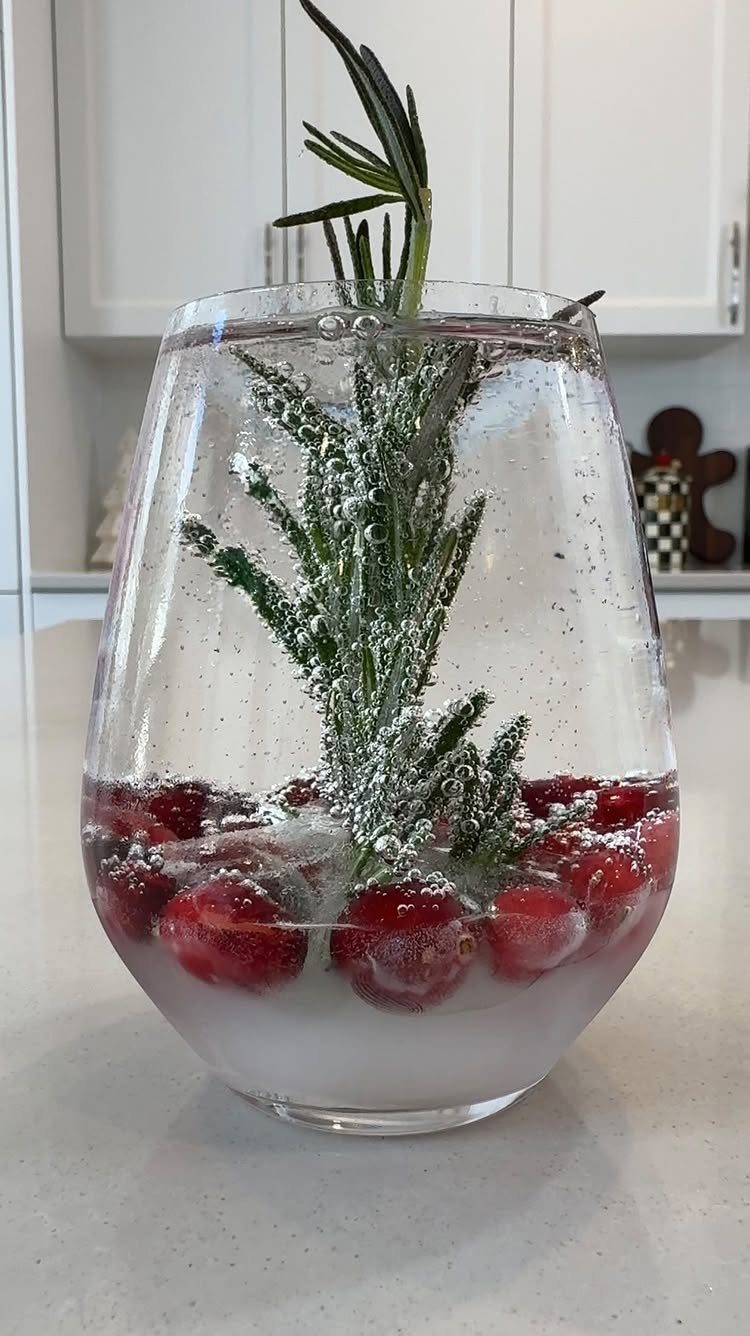 Sparkling cider in a stemless glass with fresh cranberries and a rosemary sprig.