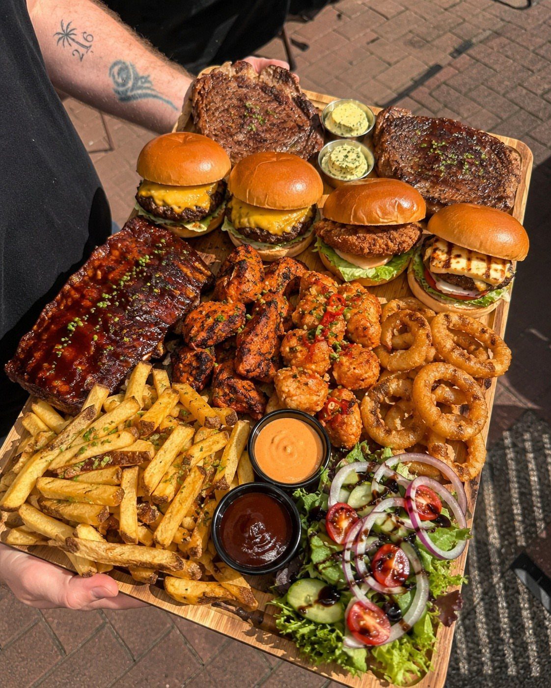 Barbecue platter on a wooden board with ribs, sliders, steaks, and fries.