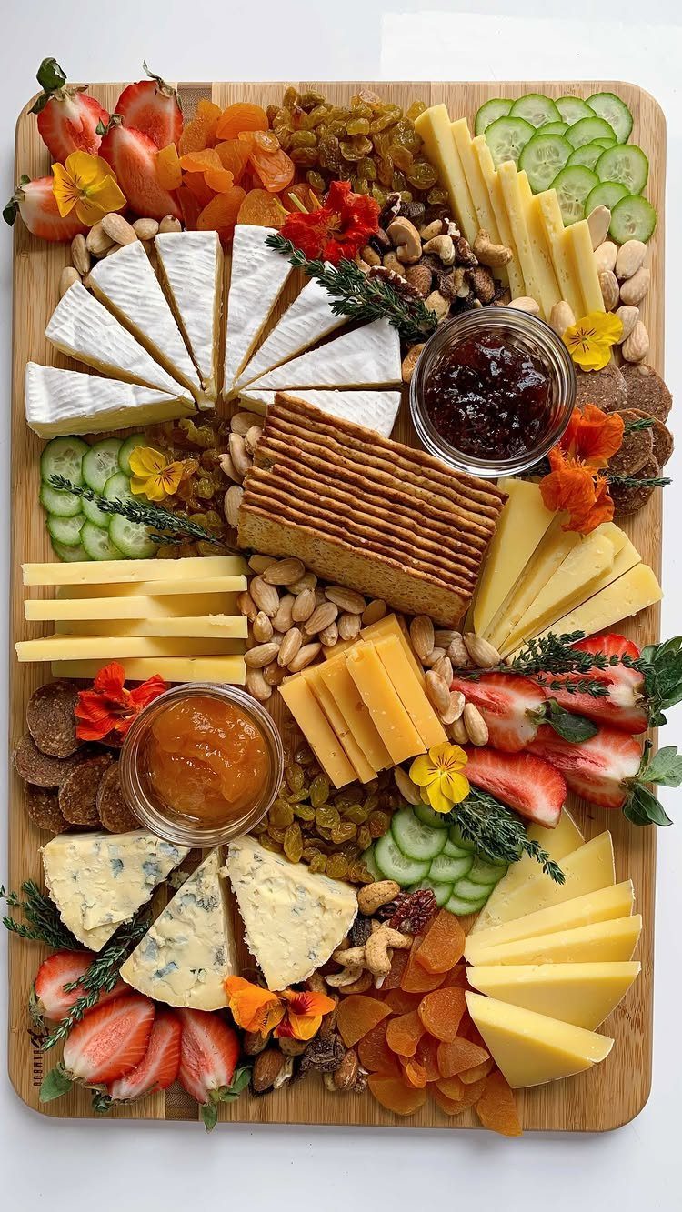 Wooden charcuterie board with various sliced cheeses, fresh fruits, vegetables, and crackers.