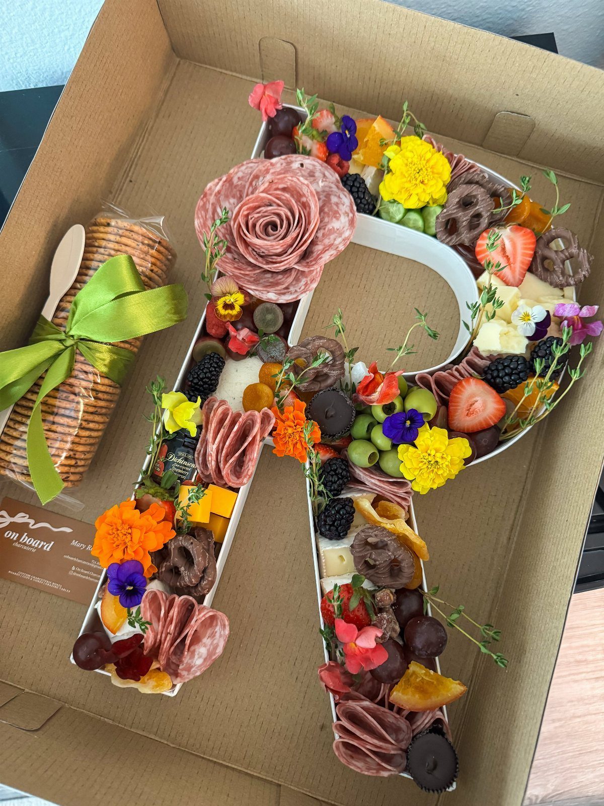 Letter A shaped charcuterie board with meats, cheeses, fruits, and fresh green herbs.