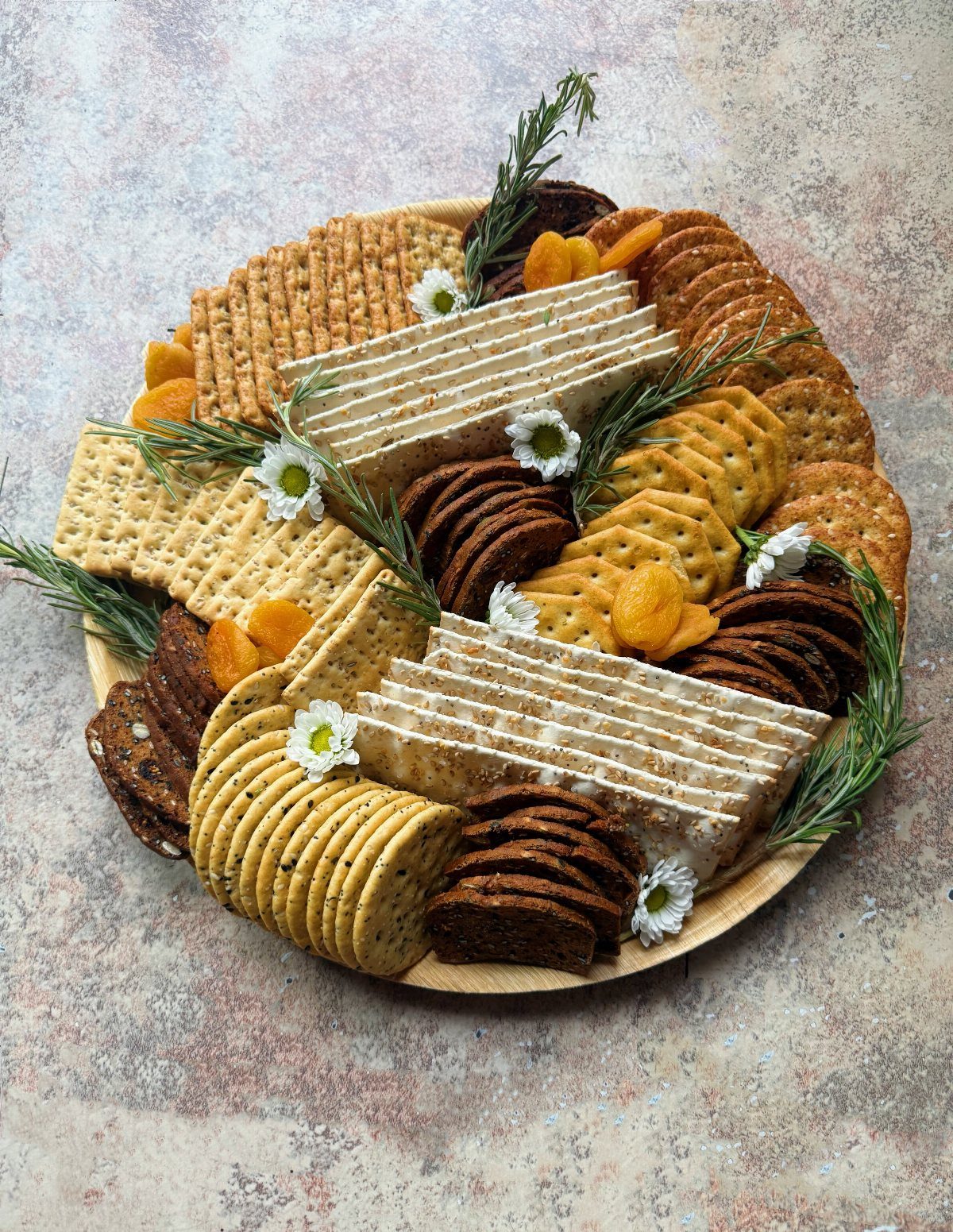 Assorted crackers and toasted breads arranged on a wooden board with dried apricots.