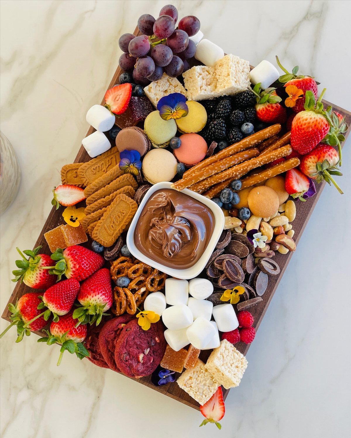 Dessert charcuterie board with fresh berries, macarons, marshmallows, and chocolate dip on wood.