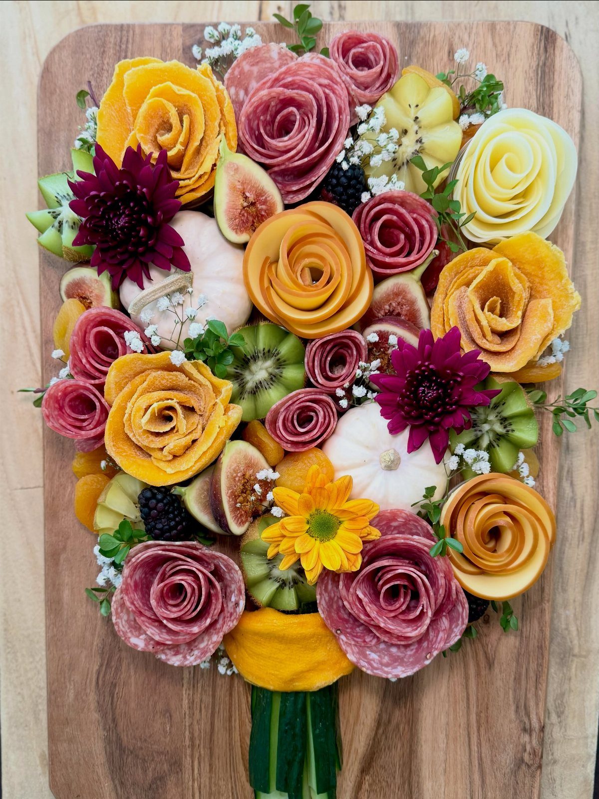 Charcuterie board arranged as a bouquet with meat roses, fruits, and small pumpkins.