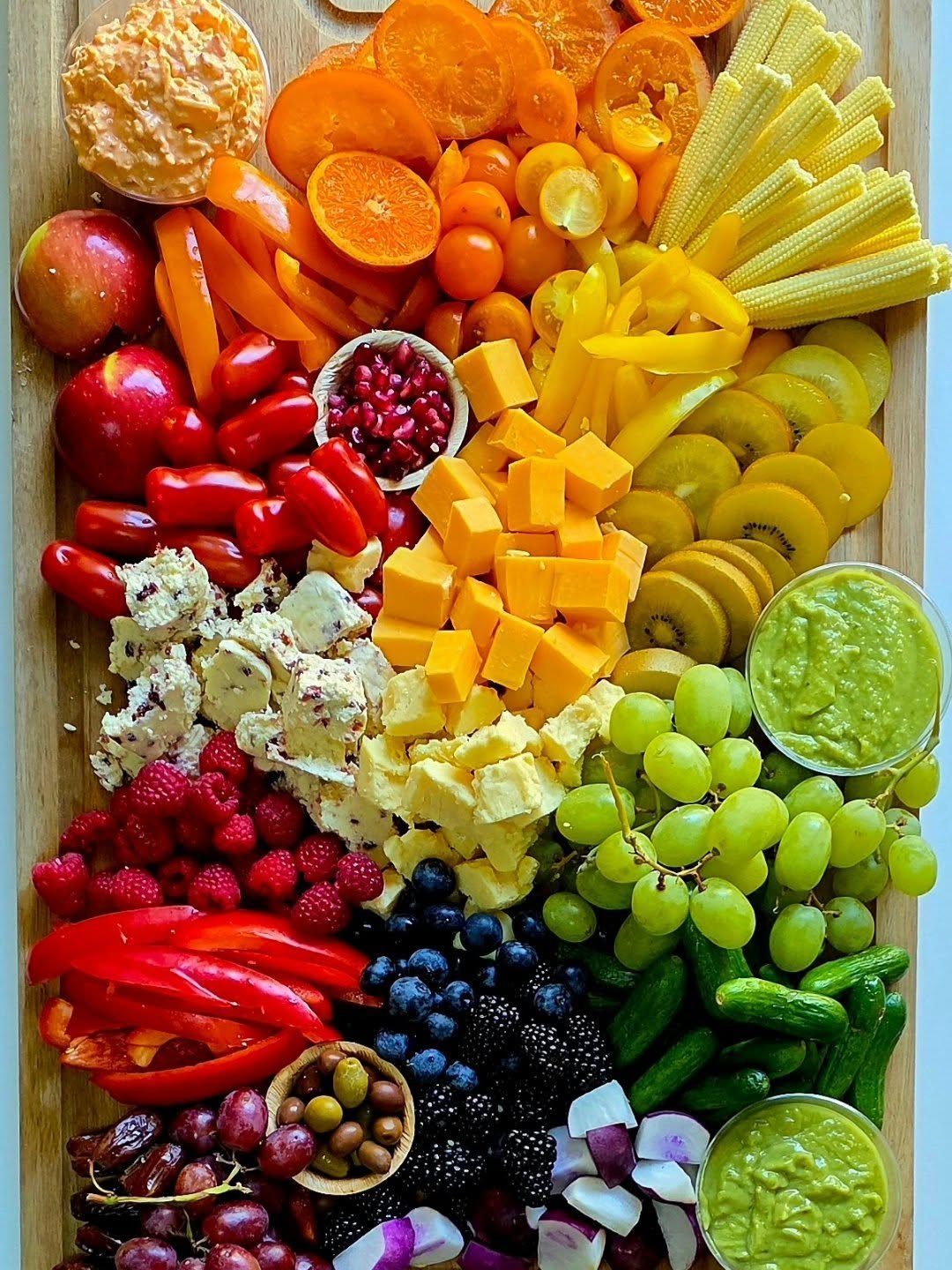 Rainbow charcuterie board with colorful fruits, vegetables, and cheeses arranged by color gradient.