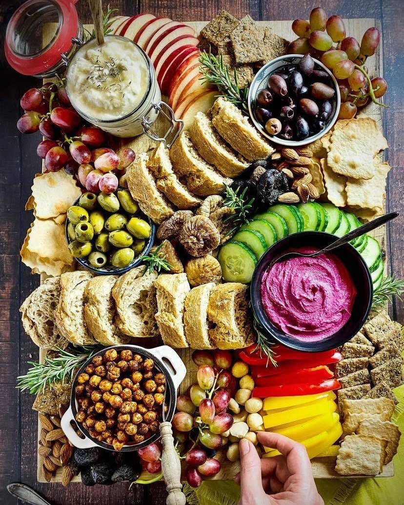 Vegan charcuterie board with fresh vegetables, fruits, sliced bread, olives, and colorful dips.