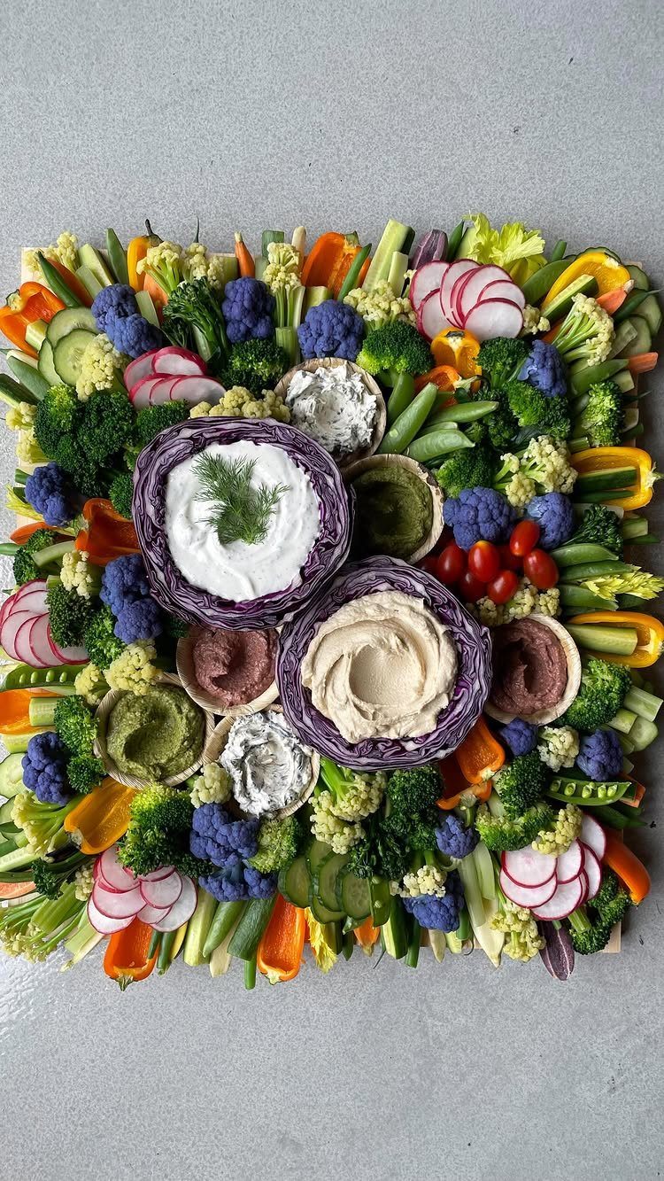 Vegetable platter with various raw vegetables and dips in purple cabbage bowls.