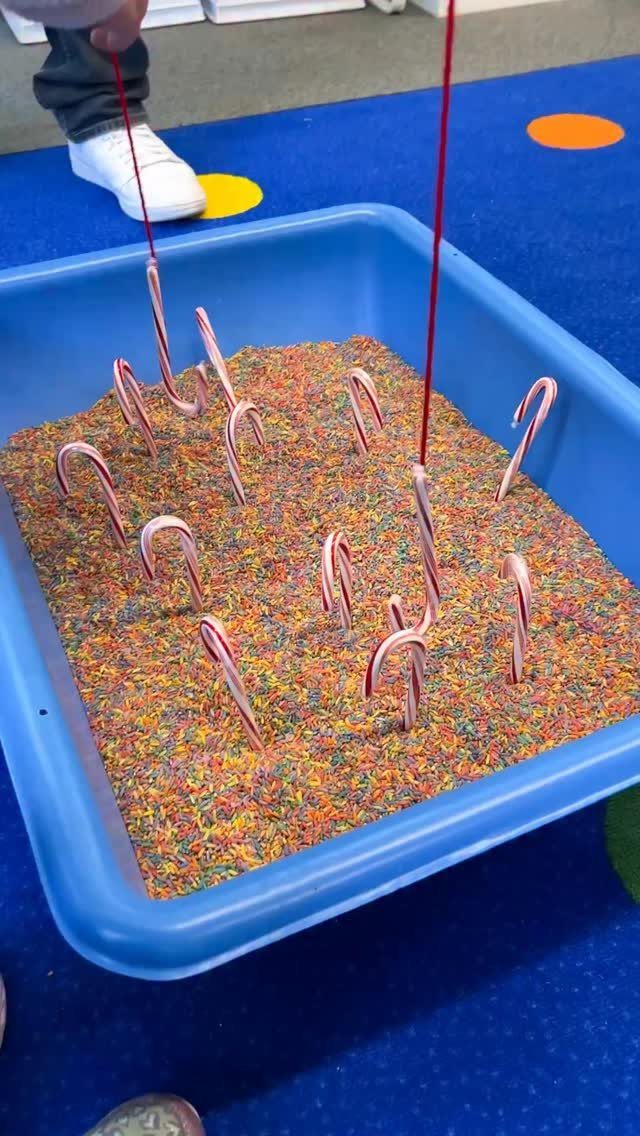 Candy canes stuck in colorful rice inside a blue bin for a game.