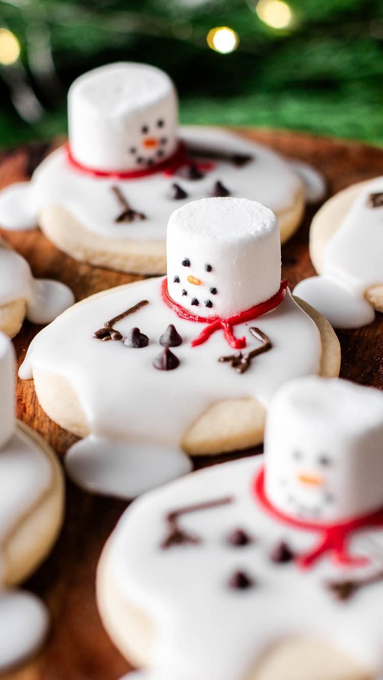 Melting snowman sugar cookies with marshmallow heads and red scarves on wooden board