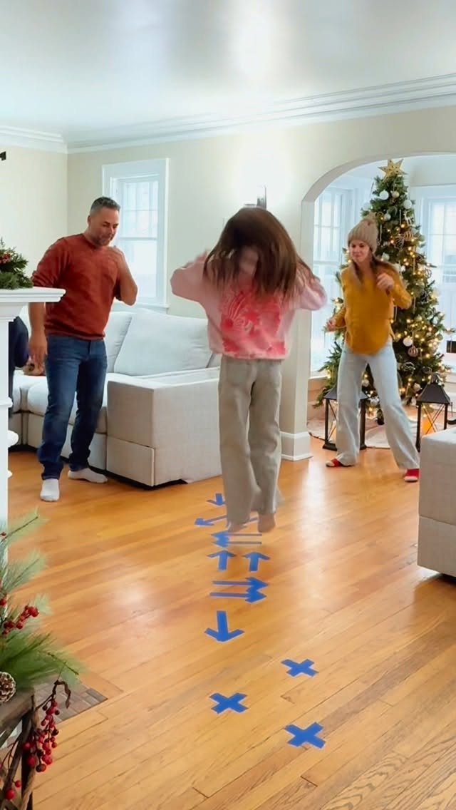 Woman jumping on blue tape markers on a wooden floor during Christmas games.