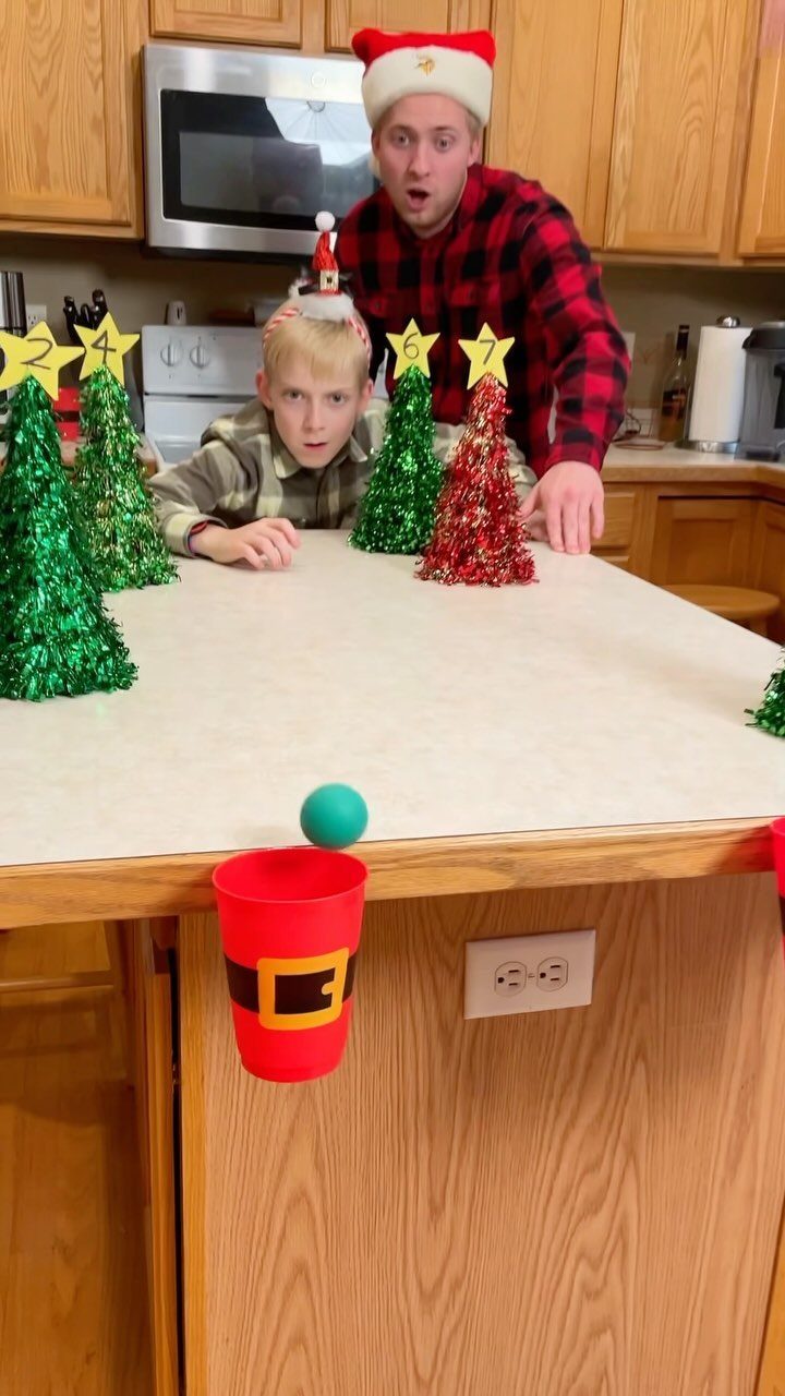 Man and boy watching a blue ball bounce toward a Santa cup.