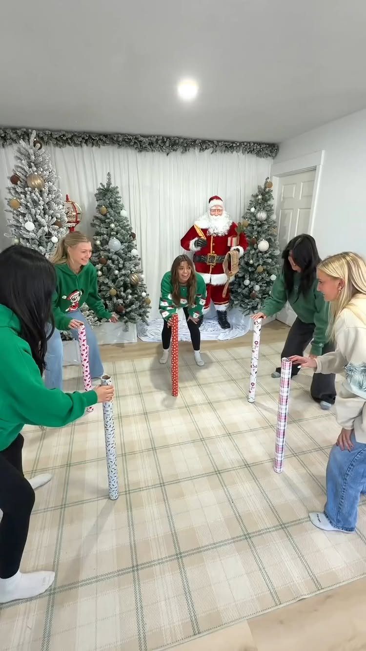 Young women and Santa Claus playing a game with wrapped gift tubes indoors.