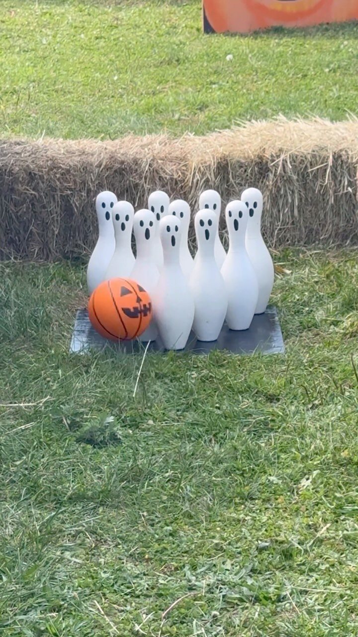 White ghost figurines and an orange pumpkin ball on a grassy field.