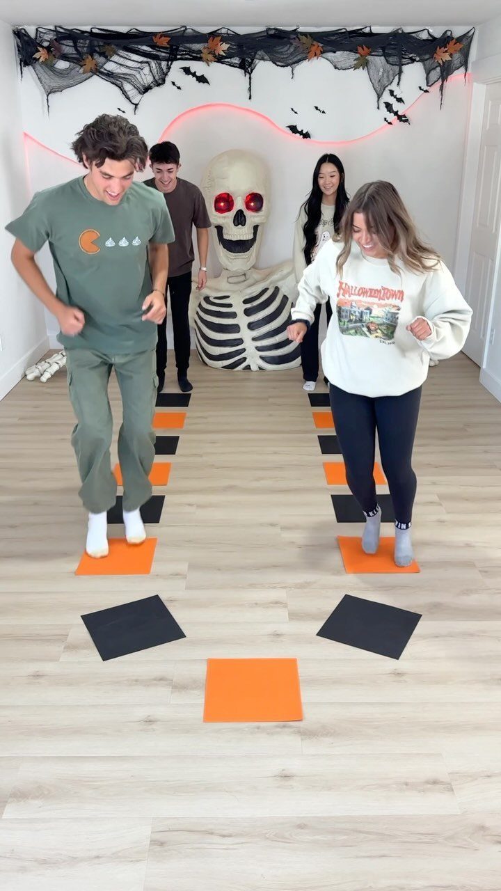 Young adults jumping on orange and black mats for a Halloween party game.
