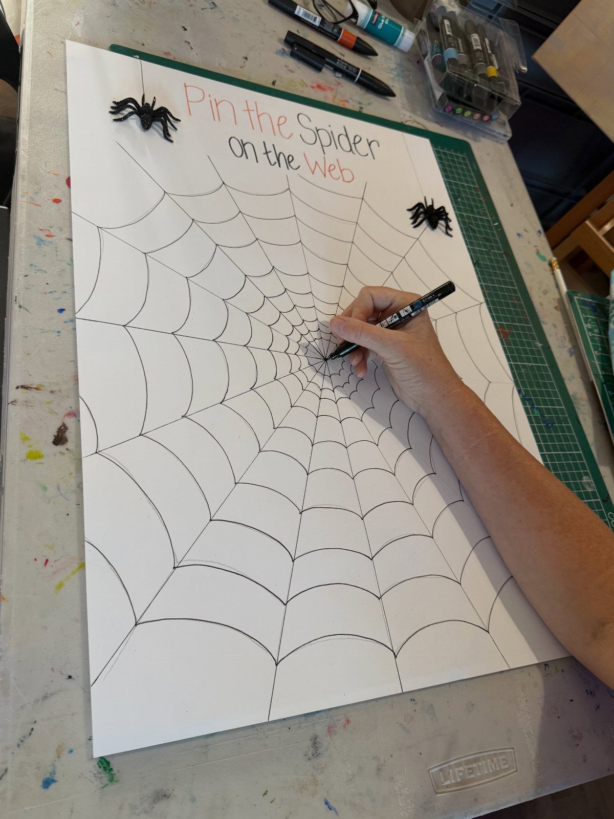 Hand drawing a spider web on a poster for Pin the Spider game.