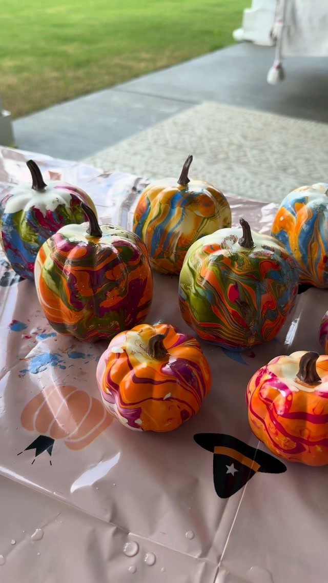 Colorful marbled painted pumpkins sitting on a white plastic tablecloth outdoors.