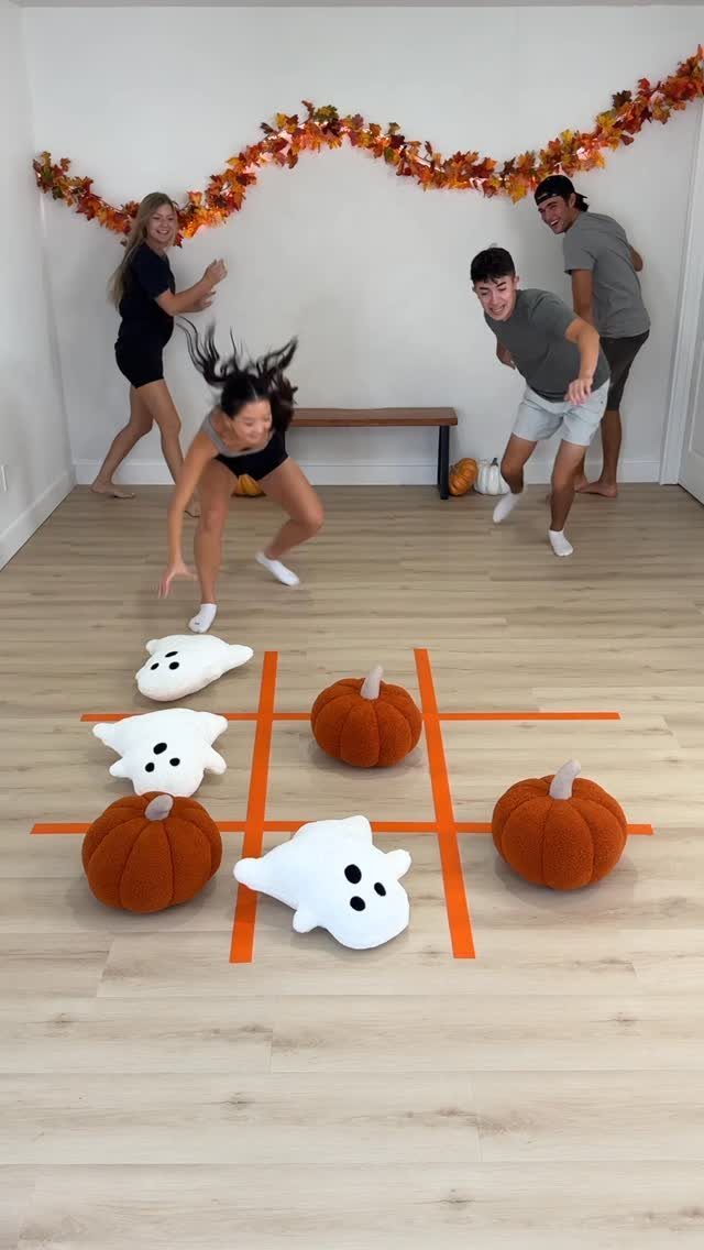 Young adults playing pumpkin and ghost tic-tac-toe on a wooden floor.