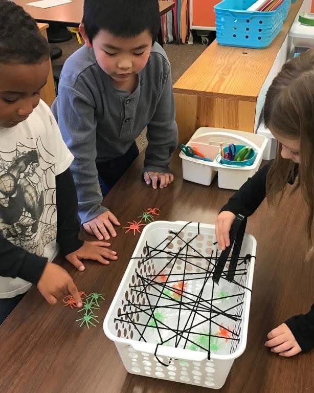Children using tongs to pick up plastic spiders from a string web basket.