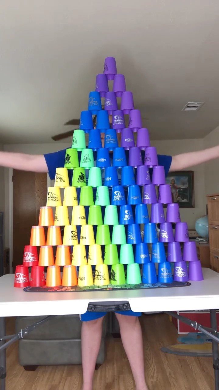 Rainbow colored plastic cups stacked in a large pyramid shape on a white table.