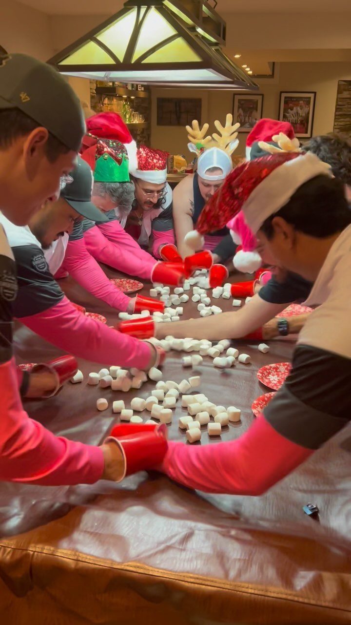 People wearing Santa hats and red oven mitts moving marshmallows on a table.