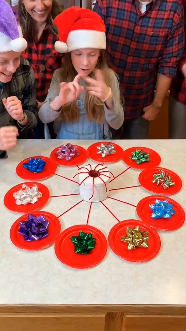 Girl in Santa hat playing a Christmas party game with red plates and bows.